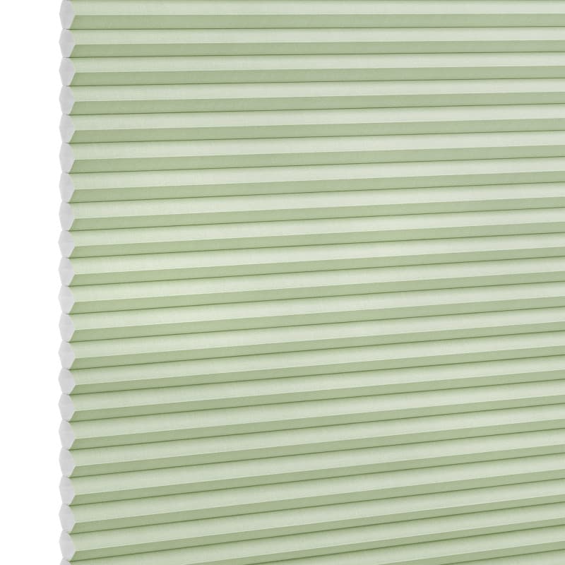 Pale green honeycomb (cellular) blind with visible hexagonal cells at left, fully lowered and closed, softly filtering light; studio-lit product shot on a white background.