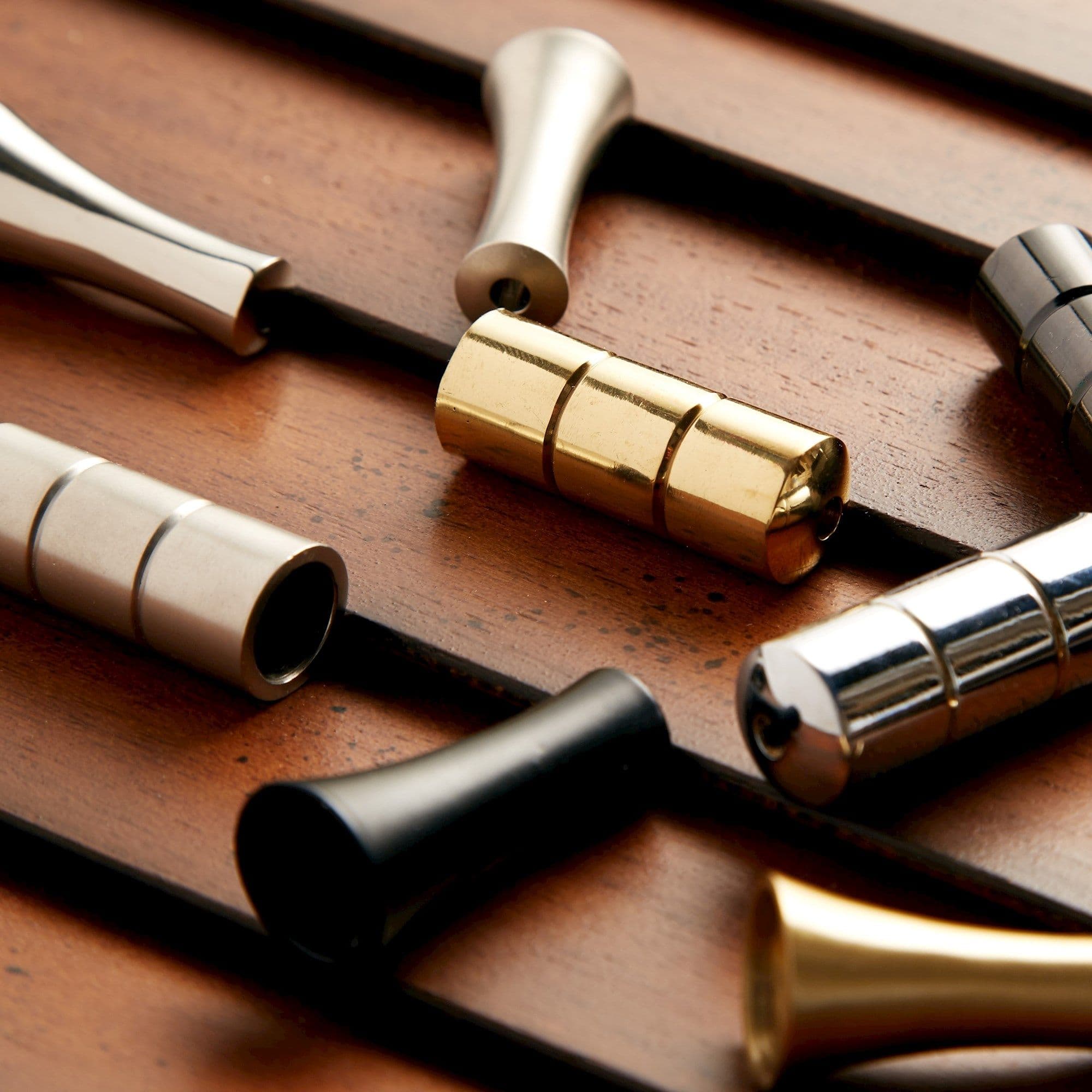 Polished cylindrical metal beads (gold, silver, black) strung on parallel dark rods, sliding along them; set on a warm wooden board under soft directional lighting with shallow focus.