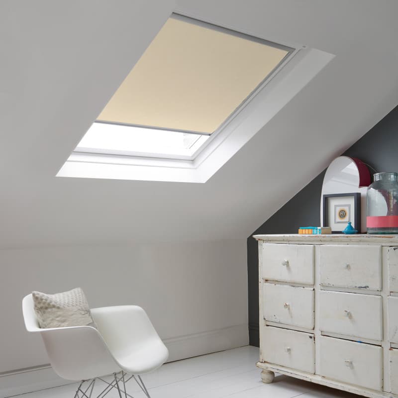 Room with white eaves wall, dark blue-grey wall to right with a shabby chic white drawer unit, a contemporary white chair, white painted floorboards and a skylight blind in pale cappucino.