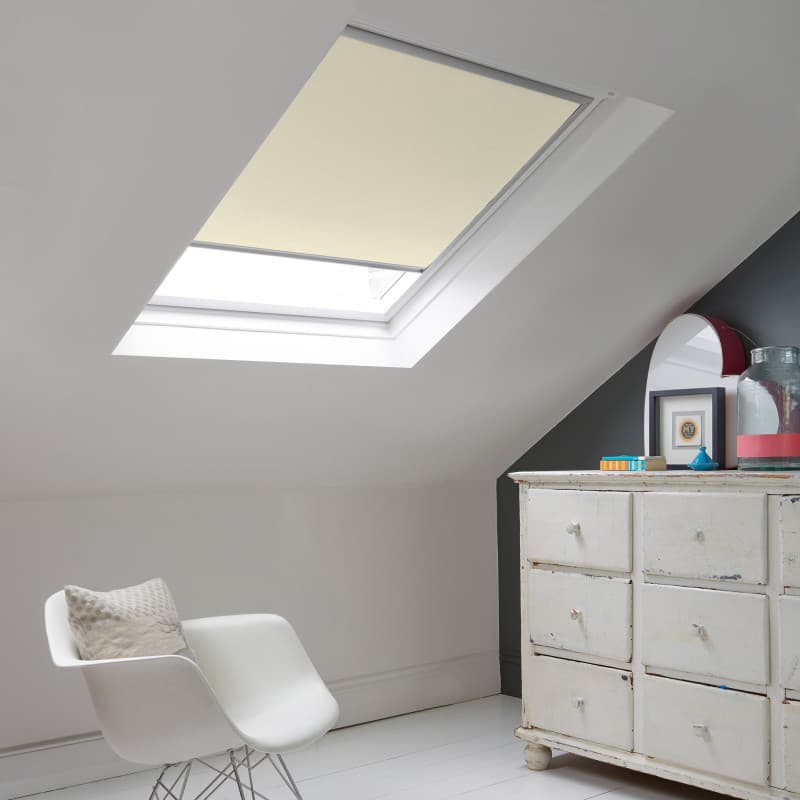 Room with white eaves wall, dark blue-grey wall to right with a shabby chic white drawer unit, a contemporary white chair, white painted floorboards and a skylight blind in almond.