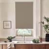 A beige roller blind covers a window above a stainless sink, partially lowered; modern kitchen countertop holds a faucet, bowls of leafy vegetables, potted plants, framed sketch, and wooden cabinets.
