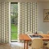 Floor-length beige-and-white patterned curtains hang on either side, parted to reveal a narrow four-pane window; dining room with wooden table and cream chairs, soft daylight and a green garden outside.