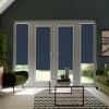 French glass doors with navy roller blinds partially lowered, showing garden light below; glass coffee table holding candles and plants sits on chevron rug, flanked by green armchairs.