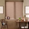 Beige horizontal venetian blinds over a recessed window, fully lowered and closed, gently filtering daylight; surrounding warm sitting area with wooden chair, console table, lamp and small decorative objects.