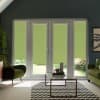 French glass doors fitted with partially lowered green roller blinds, filtering daylight into a contemporary living room with olive armchairs, a glass coffee table on a zigzag rug, and garden outside.