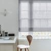 Sheer gray Roman shade (window dressing), lowered mid‑window and softly filtering daylight; simple white home office context with a wooden chair, desk, small pendant lamp and books.