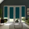 Glass patio doors with teal blinds lowered mid-height, admitting light; a glass coffee table on a chevron rug before them in a living room with green armchairs and plants.
