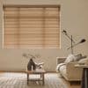 Beige horizontal venetian blinds lowered and closed, softly filtering daylight — in a neutral living room with a sofa, wooden coffee table with a vase and open book, geometric rug.