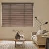 Horizontal blinds covering a wide window, slats closed with thin light lines; filtering muted daylight into a neutral living room with beige sofa, wooden table, rug, and floor lamp.