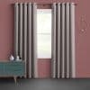Grommet-top beige floor-length curtains, hung in even folds on a metal rod and partially open, filtering soft daylight through a white-trim window in a muted-rose living room.