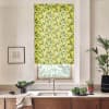 Yellow lemon-patterned roller blind covers a window, filtering light above a sink on a marble countertop; stainless faucet, potted plants, bowl of greens, and framed sketch in bright kitchen.