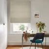 Beige fabric Roman blind, fully lowered with soft horizontal folds, filtering daylight over a sash window; home office desk with mirror, vase of flowers and teal chair, sunlit garden beyond.