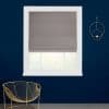 Grey fabric Roman shade lowered with visible folded tiers, filtering daylight; set in a white-framed window on a deep navy wall above a gold wire chair and circular wall sconce.