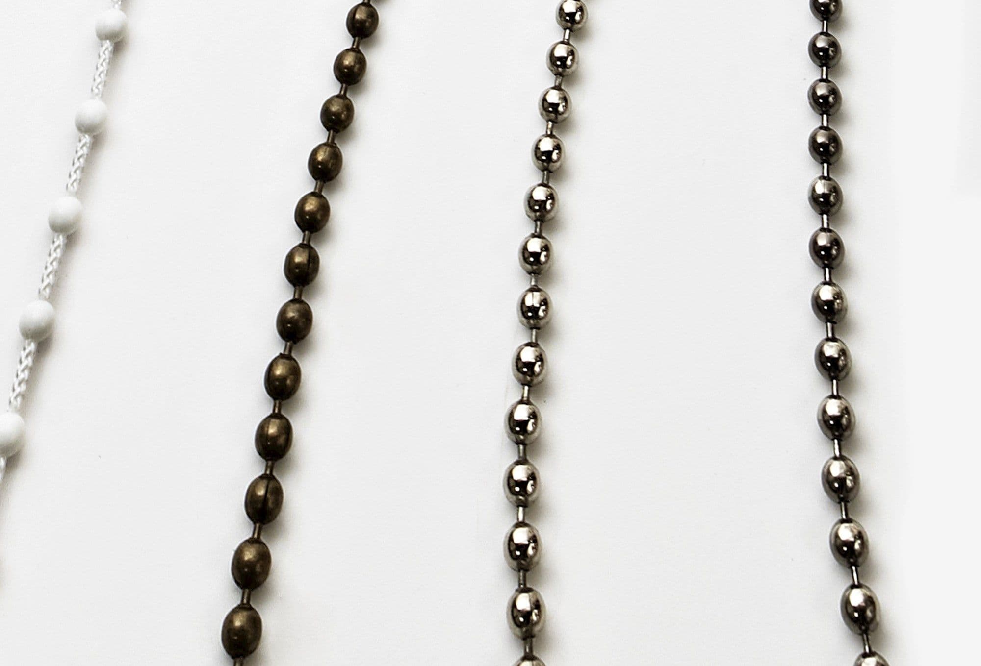 Beaded blind pull chains: a white braided cord with white beads, an antique-bronze bead chain, and two polished chrome bead chains—hanging vertically, closely spaced against a plain white backdrop, studio-lit.