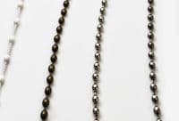 Beaded blind pull chains: a white braided cord with white beads, an antique-bronze bead chain, and two polished chrome bead chains—hanging vertically, closely spaced against a plain white backdrop, studio-lit.