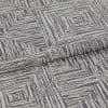 Folded woven fabric featuring a repeating distressed concentric-square pattern; a folded edge overlaps, lying flat on a neutral surface under soft, even studio lighting.