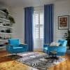 Blue grommet-top curtains flank a window with white plantation shutters, hanging open and filtering daylight; mid-century turquoise armchairs face each other on a zebra rug in a bright living room.