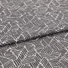 Folded patterned fabric: gray-and-white geometric print of short parallel stripes forming irregular polygons, folded across the middle. Close-up on flat surface with even studio lighting.