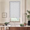 Floral roller blind partially lowered over the window, diffusing light; above a kitchen sink with faucet, marble countertop holding bowl of greens, potted plants, towel and framed sketch.