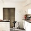 Horizontal Venetian blinds covering a recessed window, fully lowered and closed, filtering light; modern white kitchen with glossy countertops, chrome stool, trash bin, wall clock and vase of red tulips.