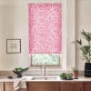 Pink floral roller blind hangs lowered over a window, filtering light above a kitchen sink and counter with faucet, bowls of greens, framed sketch left and tall potted plant right.