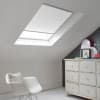Room with white eaves wall, dark blue-grey wall to right with a shabby chic white drawer unit, a contemporary white chair, white painted floorboards and a skylight blind in white.