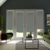 French doors with gray roller blinds partially lowered, blocking light while revealing garden; set in a modern living room with green armchairs, glass coffee table on a black-and-white chevron rug.