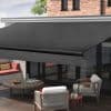 Dark charcoal retractable awning, mounted above glass doors with roller bar, extended and shading the seating area; outdoor wooden-deck patio attached to a brick house, cushioned chairs and round table.
