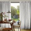 White pleated curtains with multicolored star print, pulled aside at center to frame a glass door and admit daylight; wooden dining table set for breakfast and leafy backyard beyond.