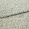 Beige speckled woven fabric upholstery swatch folded once, overlapping edge visible; close-up showing textured weave and low pile, neutral studio lighting on a flat surface.