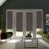 Glass double doors with lowered dark roller blinds stand closed, framing narrow garden glimpses; living room contains green armchairs, glass coffee table on chevron rug and potted plants.