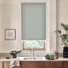 Roller blind lowered over a window above a double-basin sink, blocking light; wooden countertop and cabinets flank a faucet, with bowls of leafy vegetables, potted plants, and framed sketch nearby.