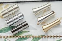 Metal curtain-rod components — three segmented chrome connectors (left) and three flared cone finials in silver and gold (right) — lie arranged on white leaf-print fabric under soft overhead light.