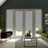 Double glass patio doors with sidelights are fitted with partially lowered white roller blinds in a contemporary living room with green armchairs, glass coffee table, chevron rug, and garden.