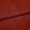 Rust-red textured boucle fabric folded across the frame, creating a dark seam; close-up studio view highlighting coarse looped surface and even, warm lighting.