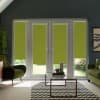 French patio doors with four lime-green roller blinds partially lowered, framing a sunlit garden beyond; contemporary living room contains green velvet armchairs, glass coffee table, chevron rug, and wall art.
