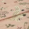 Pink woven fabric printed with red-crowned cranes and stylized trees — folded to show layered panels — close-up on a soft textile surface under soft, even lighting.