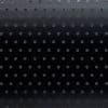Black roller blind with regular small circular perforations — lowered and closed, the holes subtly admit faint light — set in a dim interior against a smooth background with a gentle top gradient.