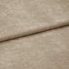 Beige textured fabric folded diagonally, overlapping along a soft crease — close-up of a chenille-like upholstery or curtain textile with subtle ribbed pile, even neutral lighting on a flat surface.