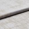 A folded plush velvet-like upholstery fabric with a mottled beige and off-white pattern is layered to reveal pile and edge, shown close-up on a neutral surface under soft studio lighting.