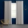 Grommet-top light gray curtains, hung on a black rod and parted to frame a bright window; modern navy-painted room with a gold wire chair and circular wall shelf.