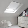 Room with white eaves wall, dark blue-grey wall to right with a shabby chic white drawer unit, a contemporary white chair, white painted floorboards and a skylight blind in white.