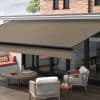 A brown retractable fabric awning with a straight valance, fully extended over glass patio doors, shading a wooden-deck seating area with chairs and a coffee table against a brick house in daylight.