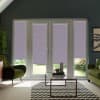 Patio doors with lilac geometric roller blinds covering panes, revealing a narrow garden strip; framed by green armchairs, glass coffee table, chevron rug, and indoor plants in a modern living room.