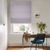 Lilac Roman blind, lowered to the sill with soft horizontal folds, filtering daylight; above desk with teal chair, mirror, vase of foliage and framed coastal print in bright study.
