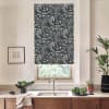Navy botanical roller blind covers window above a stainless faucet; kitchen countertop holds sink, bowl of greens, potted plants, and a framed sketch on a pale wall.