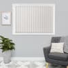 Vertical fabric blinds, beige and fully closed, cover a white-framed window, softly diffusing daylight; set in a gray living room with potted plant, framed botanical print, patterned rug and armchair.