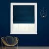 Navy Roman shade, partially lowered over a white-framed window, filtering daylight; set in a dark-blue wall with a gold chair below and a circular gold wall sconce to the right.