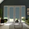 French glass doors with blue roller blinds lowered about two-thirds, framing a sunlit garden beyond; modern living room features green velvet chairs, glass coffee table and chevron-patterned rug.