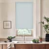 Pale blue roller blind covers kitchen window, blocking light; stainless faucet and sink below on marble countertop with wooden cabinets, bowls of greens, framed sketch left and potted plant right.